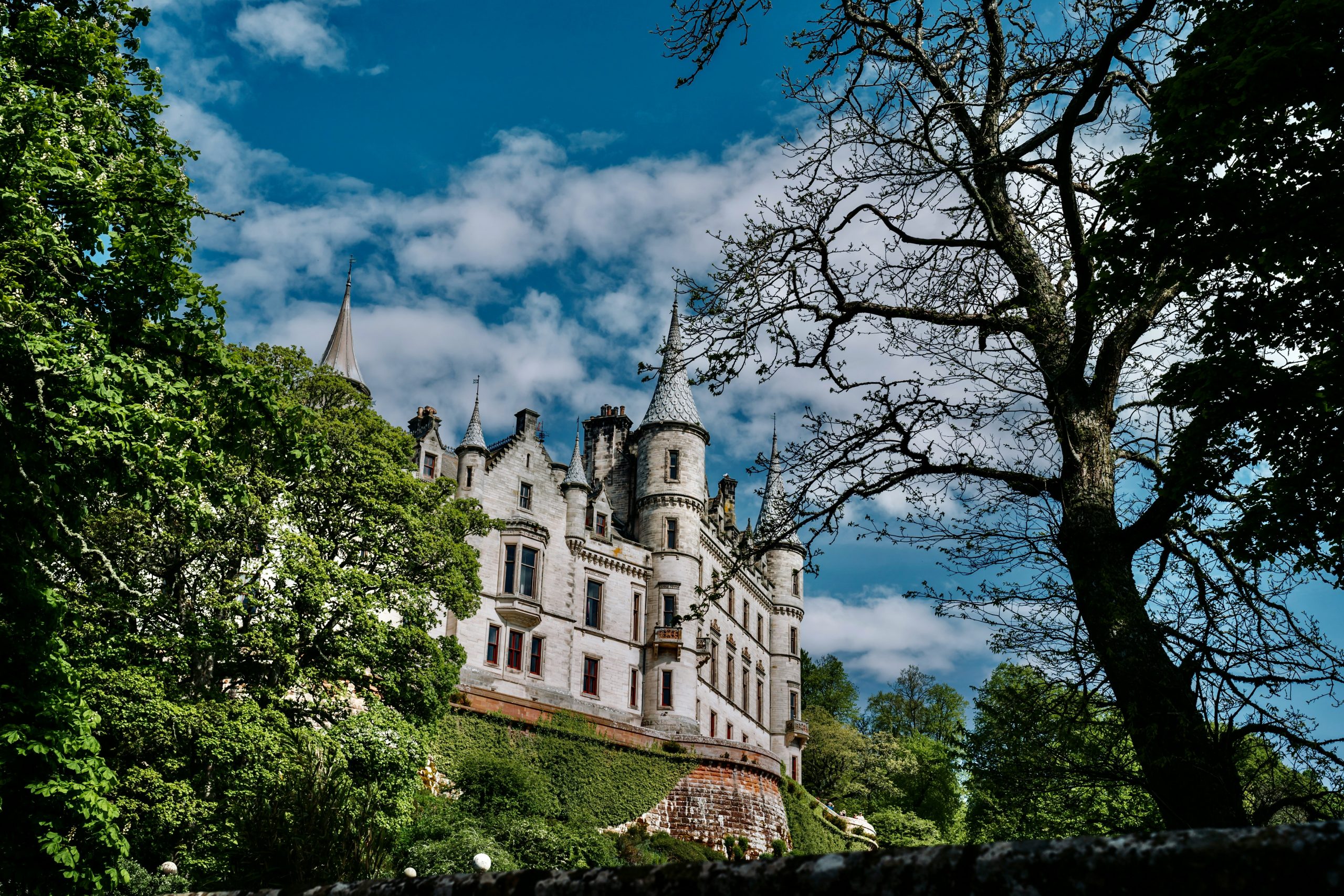 A view of a castle in Scotland through some green trees.